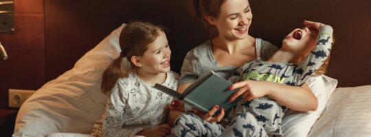 mama i dvoje djece na krevetu čitaju slikovnicu prije spavanja