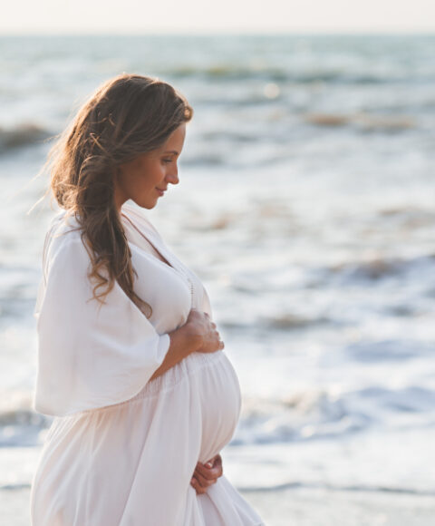 trudnica na plaži drži svoj trbuh